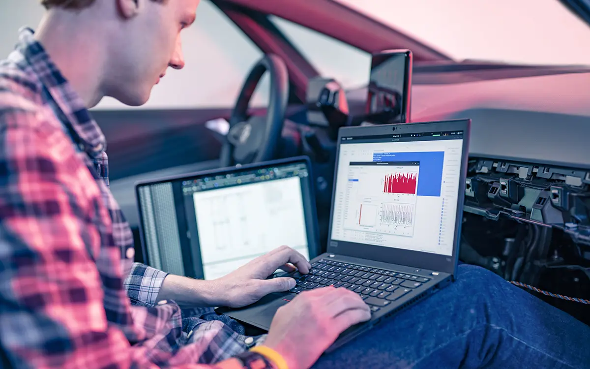 Ein Student sitzt in einem Auto und betrachtet die Messdaten auf seinem Laptop. Situation am Fachbereich Informatik der h_da, Hochschule Darmstadt. 