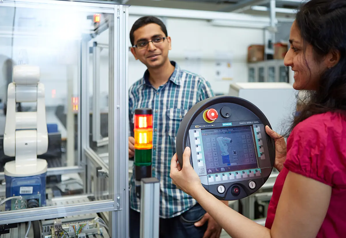 Studentin hält eine runde Steuereinheit für einen Roboter, der im Hintergrund zu sehen ist. Situation im Labor des Fachbereich MK, Maschinenbau und Kunststofftechnik der h_da, Hochschule Darmstadt. 